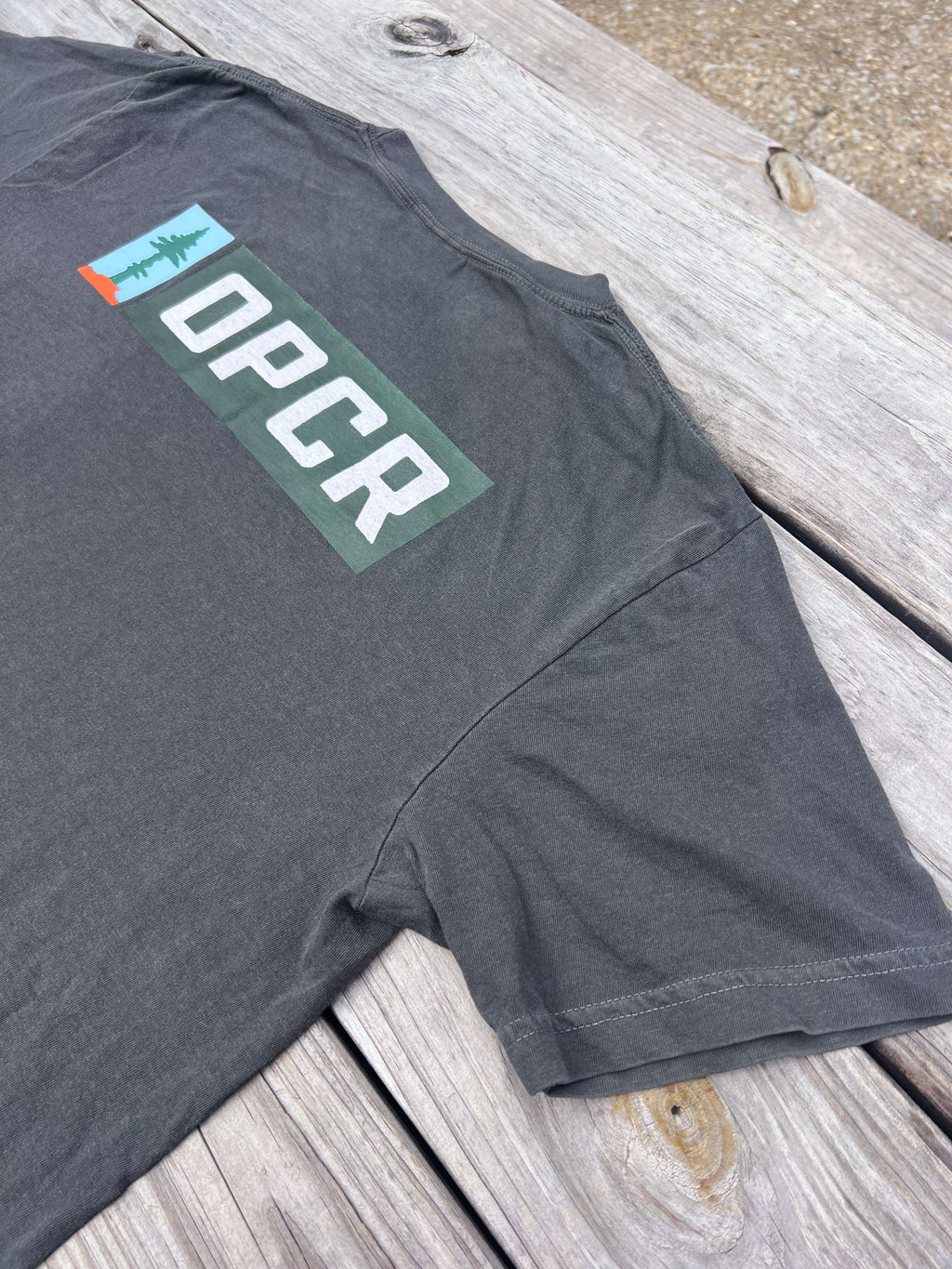 Backside of a gray t-shirt with an OPCR logo and text