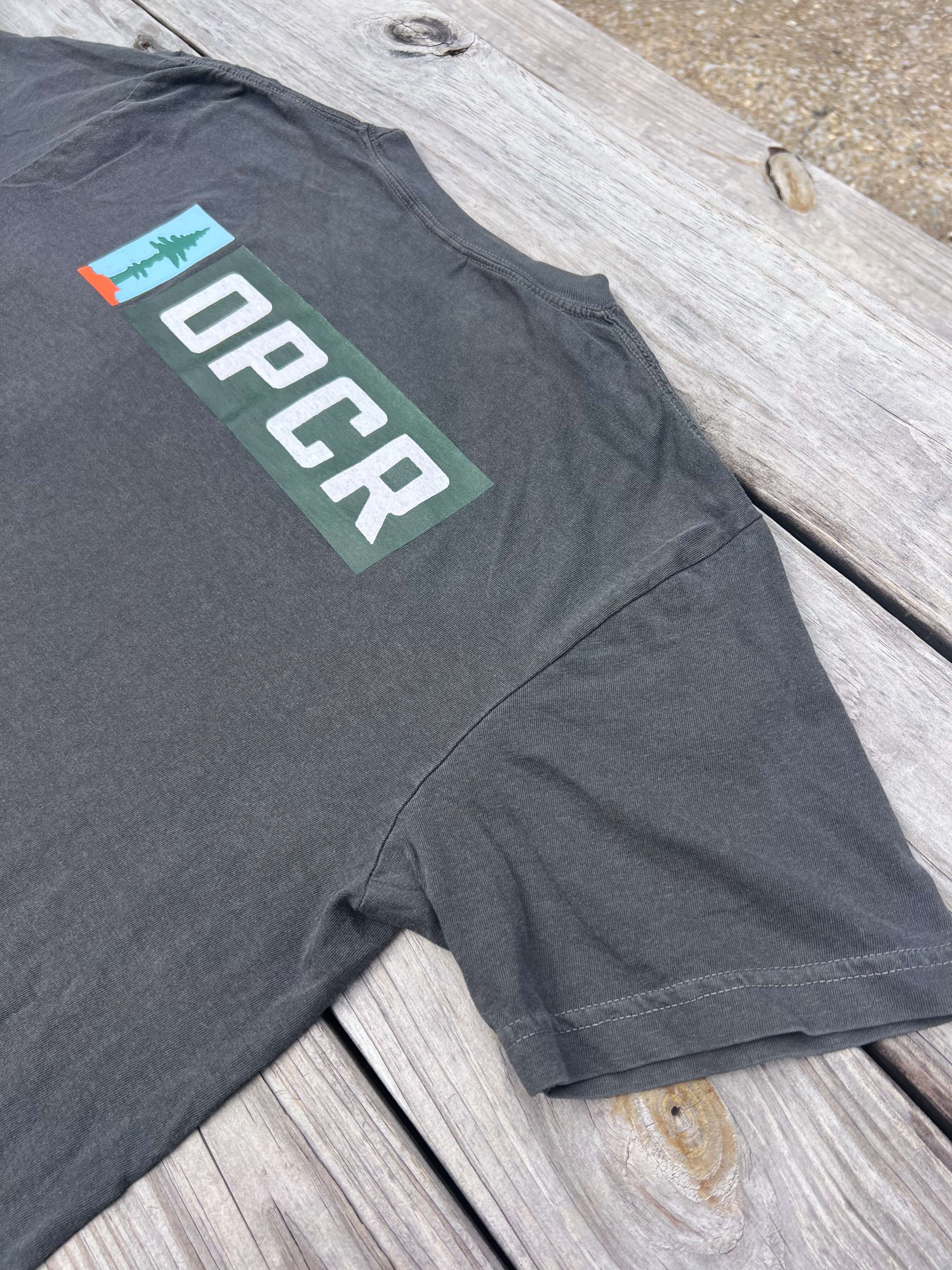 Backside of a gray t-shirt with an OPCR logo and text