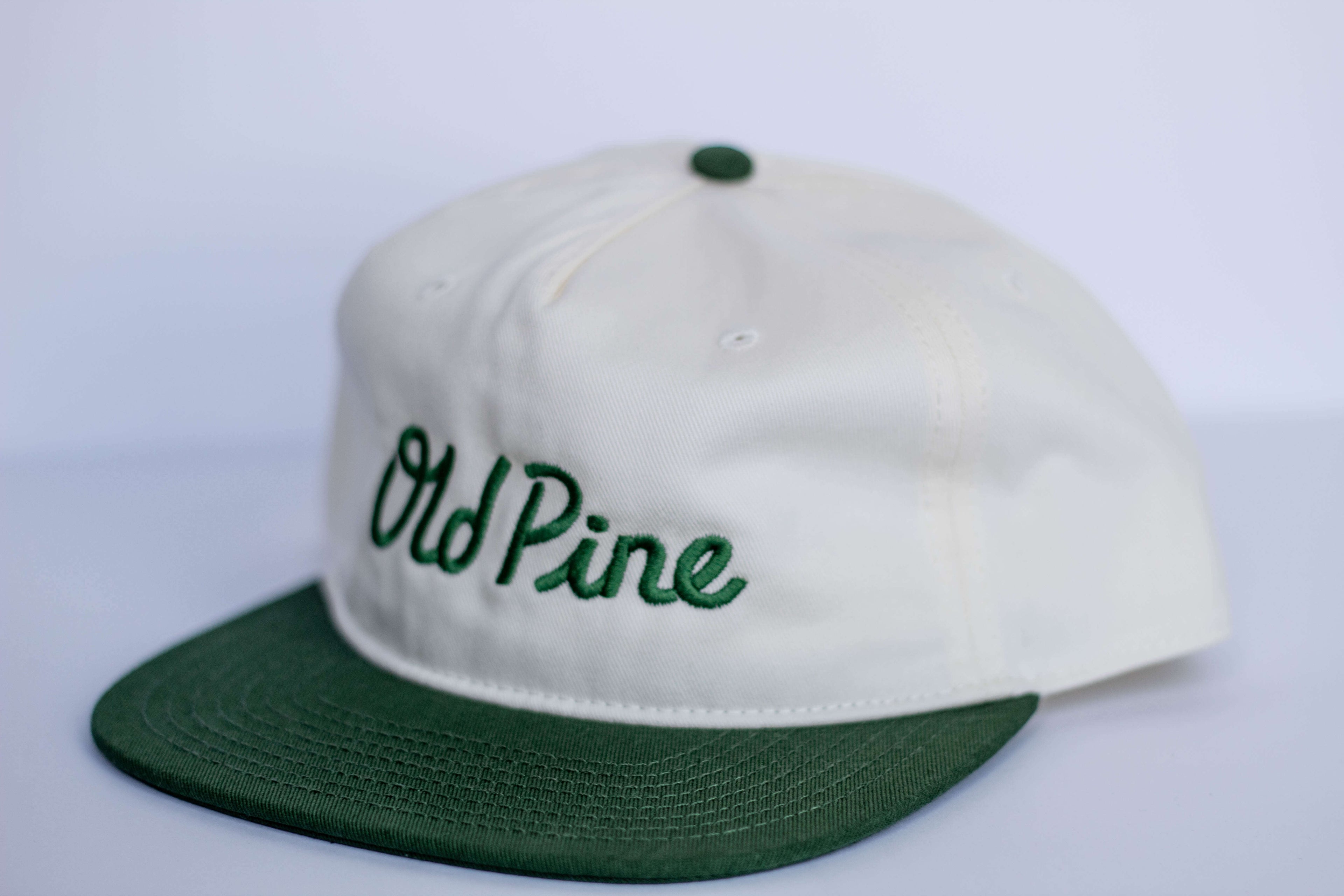White cap with green brim and 'Old Pine' text on a white background